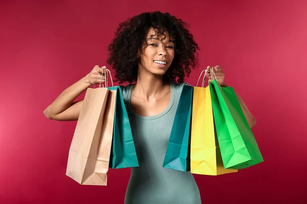 Happy African-American woman with shopping bags on color background — Stock Photo, Image