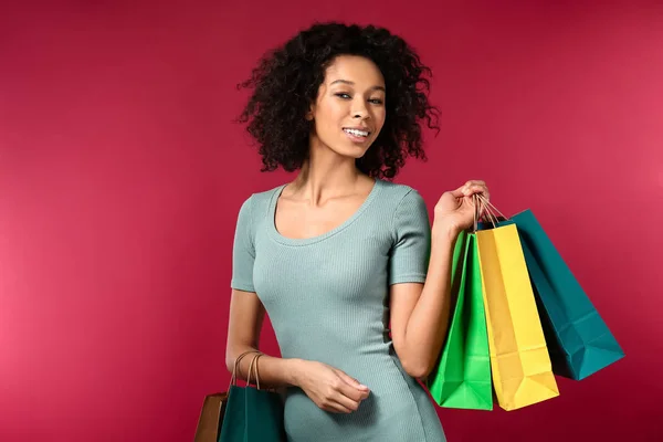 Young African-American woman with shopping bags on color background — Stock Photo, Image