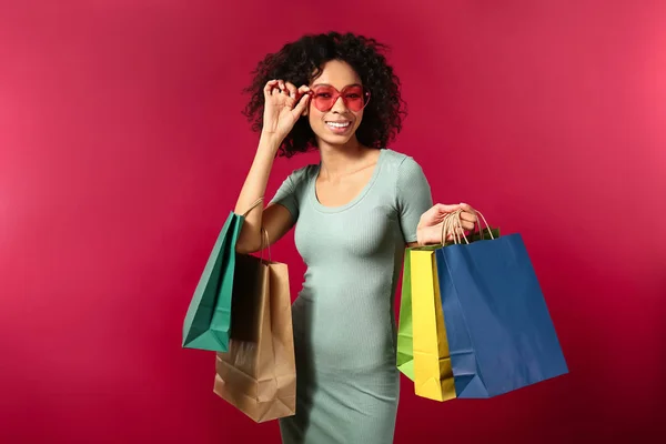 Young African-American woman with shopping bags on color background — 스톡 사진