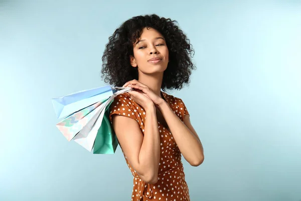 Giovane donna afro-americana con borse della spesa su sfondo colore — Foto Stock