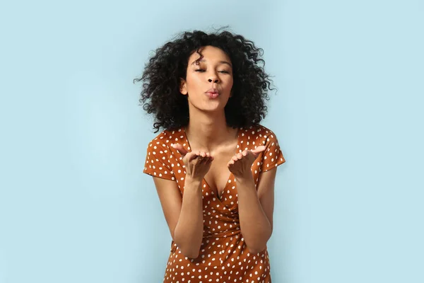 Joven mujer afroamericana soplando beso sobre fondo de color — Foto de Stock