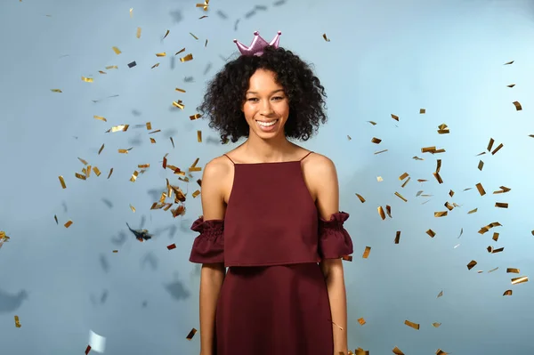 Happy African-American woman with falling confetti on color background — Stock Photo, Image