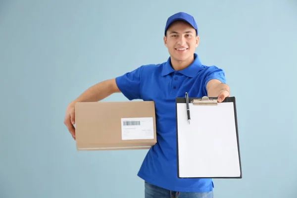 Delivery man with box and clipboard on color background