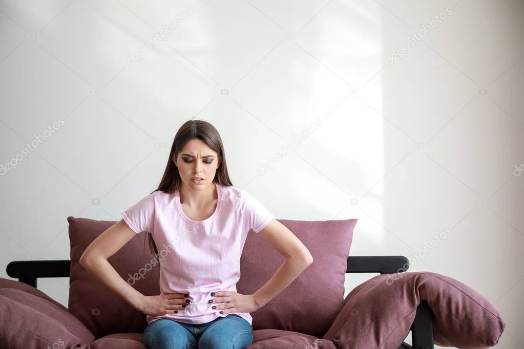Young woman suffering from abdominal pain while sitting on sofa against white background
