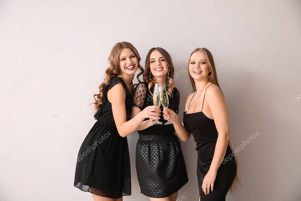 Beautiful young women with glasses of champagne on light background