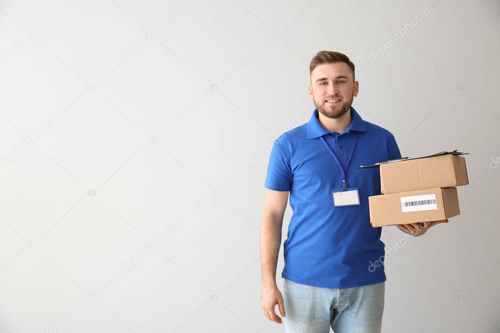 Handsome delivery man with boxes on light background