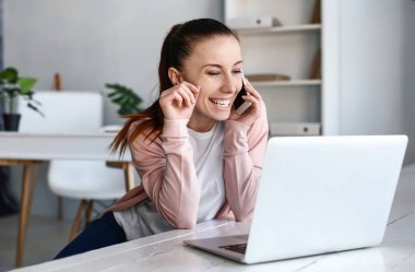 Evde dizüstü bilgisayarla çalışan bir kadın telefonla konuşuyor.