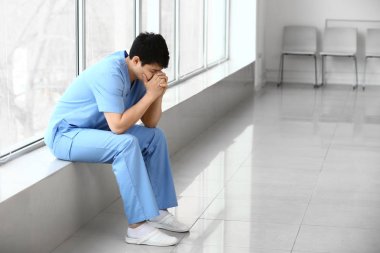 Klinikte pencere eşik üzerinde oturan depresif erkek tıbbi asistan