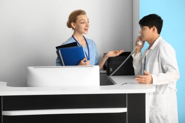 Erkek doktor klinikte resepsiyon un yanında telefonla konuşuyor