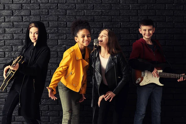 Band of teenage musicians playing against dark wall — Stock Photo, Image