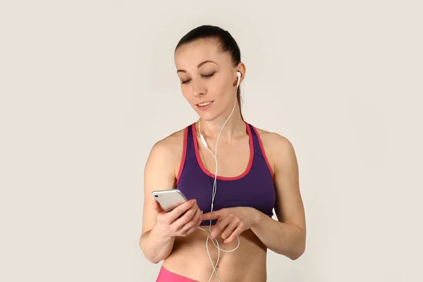 Спортивная женщина слушает музыку на светлом фоне — стоковое фото