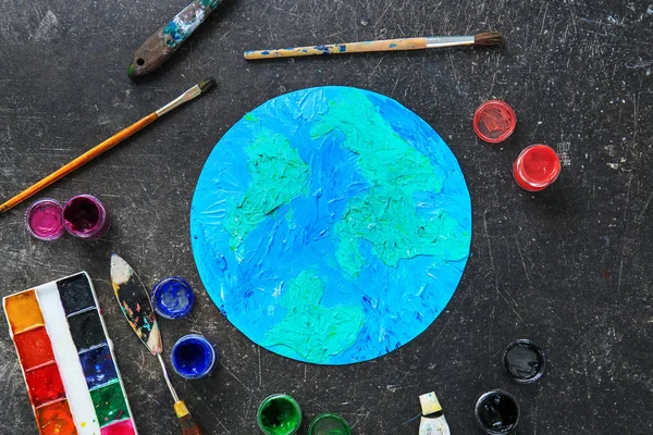 Painting of Earth with painter's supplies on dark background