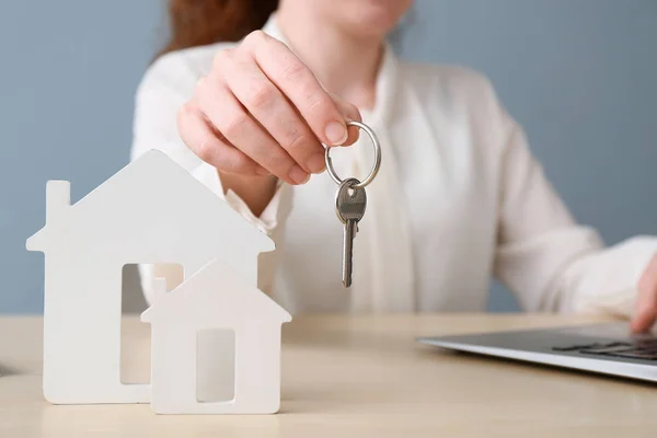 Immobilienmakler mit Schlüssel, Laptop und Häuserfiguren am Tisch — Stockfoto