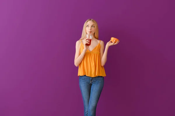 Mooie jonge vrouw met verse grapefruitsap op kleur achtergrond — Stockfoto