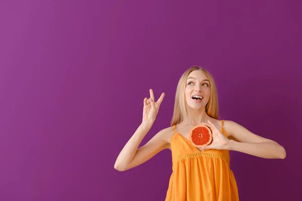Mooie jonge vrouw met verse grapefruit op kleur achtergrond — Stockfoto