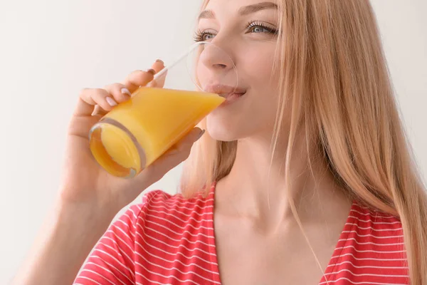 Mooie jonge vrouw het drinken van vers sap op lichte achtergrond — Stockfoto