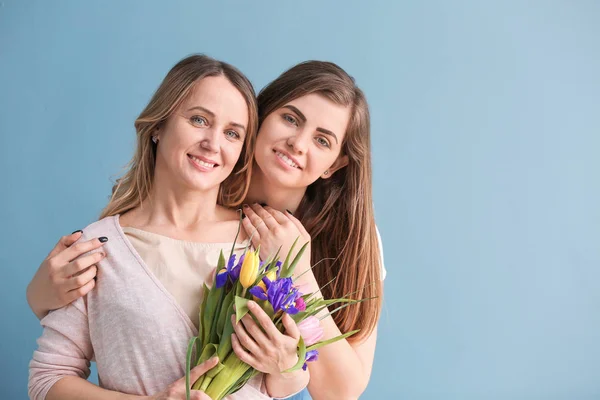 Portrait of happy mother and daughter with flowers on color background — Stock Photo, Image