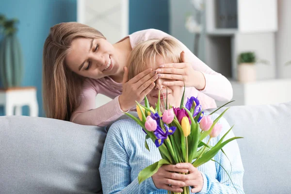 Hija saludando a su madre con flores en casa —  Fotos de Stock