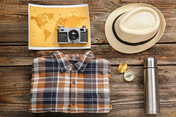 Póló, kalap, világtérkép, termosz és fotó kamera fa háttérrel. Utazási koncepció — Stock Fotó