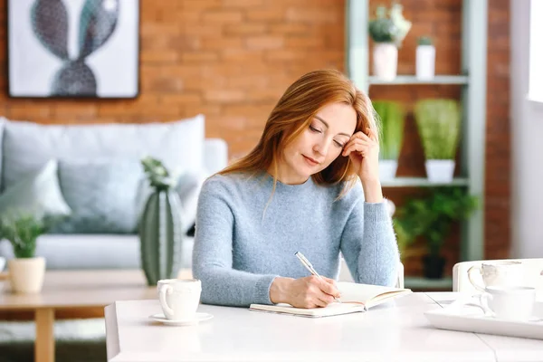 Portrait of mature woman writing in notebook at home — Stock Photo, Image