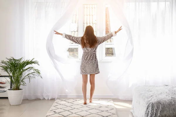 Jonge vrouw opent licht gordijnen in de slaapkamer thuis — Stockfoto