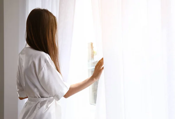 Jonge vrouw opent licht gordijnen in de slaapkamer thuis — Stockfoto