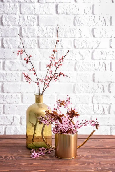 Vase and watering can with beautiful blossoming branches on table