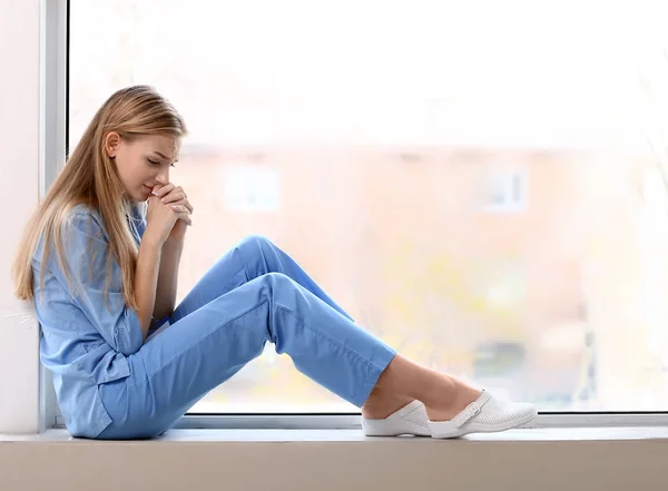 沮丧的女医疗助理坐在诊所的窗台上 — 图库照片