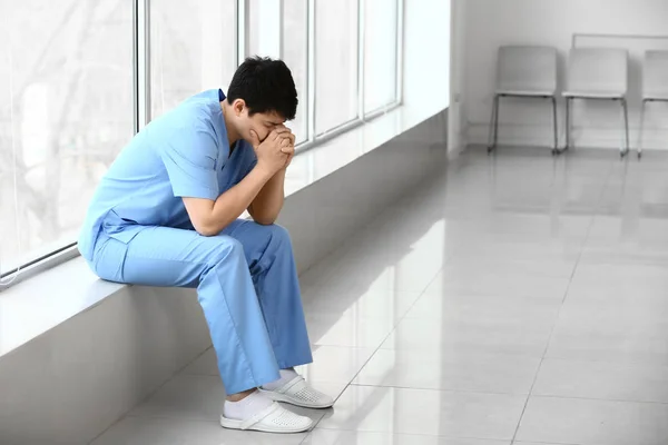 Depressed male medical assistant sitting on window sill in clinic — Stock Photo, Image