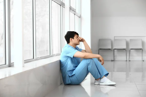 Depressed male medical assistant sitting near window in clinic — Stock Photo, Image