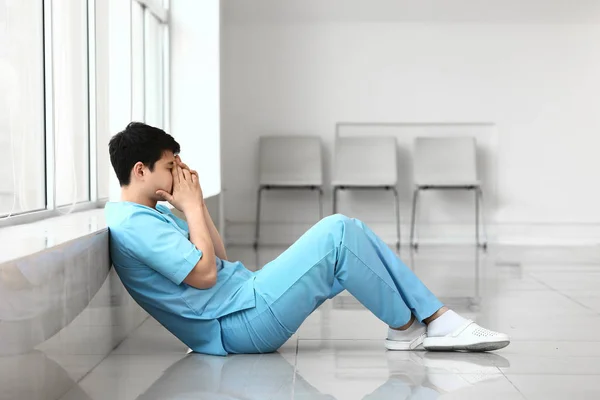 Depressed male medical assistant sitting near window in clinic — Stock Photo, Image