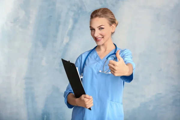 Portrait of female medical assistant showing thumb-up on color background — Stock Photo, Image