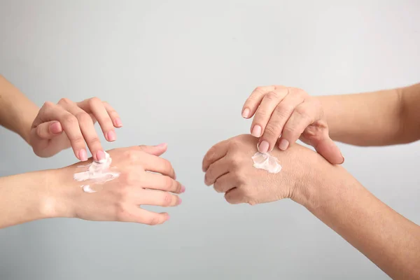 Mujeres jóvenes y maduras aplicando crema de manos sobre fondo claro —  Fotos de Stock