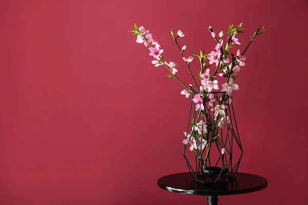 Vase with beautiful blossoming branches on table against color background — Stock Photo, Image