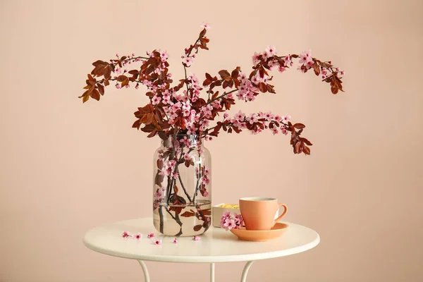 Vase mit schönen blühenden Zweigen und einer Tasse Kaffee auf dem Tisch vor hellem Hintergrund — Stockfoto