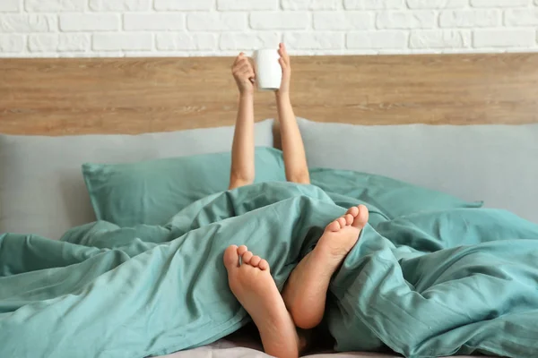 Jeune femme avec tasse de boisson chaude couchée dans le lit — Photo