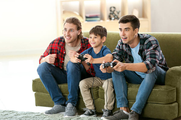 Голубая пара с усыновленным ребенком, играющая в видеоигры дома
