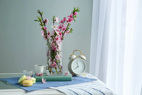 Composición con hermosas ramas florecientes, reloj, copas y sabrosos macarons en la mesa —  Fotos de Stock
