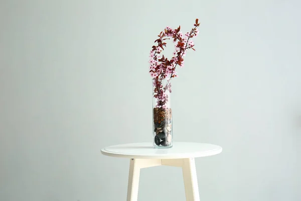 Wazon z pięknymi kwitnącymi gałęziami na stole na jasnym tle — Zdjęcie stockowe