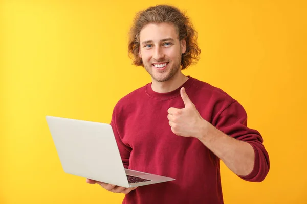 Männlicher Programmierer mit Laptop zeigt Daumen-hoch-Geste auf farbigem Hintergrund — Stockfoto