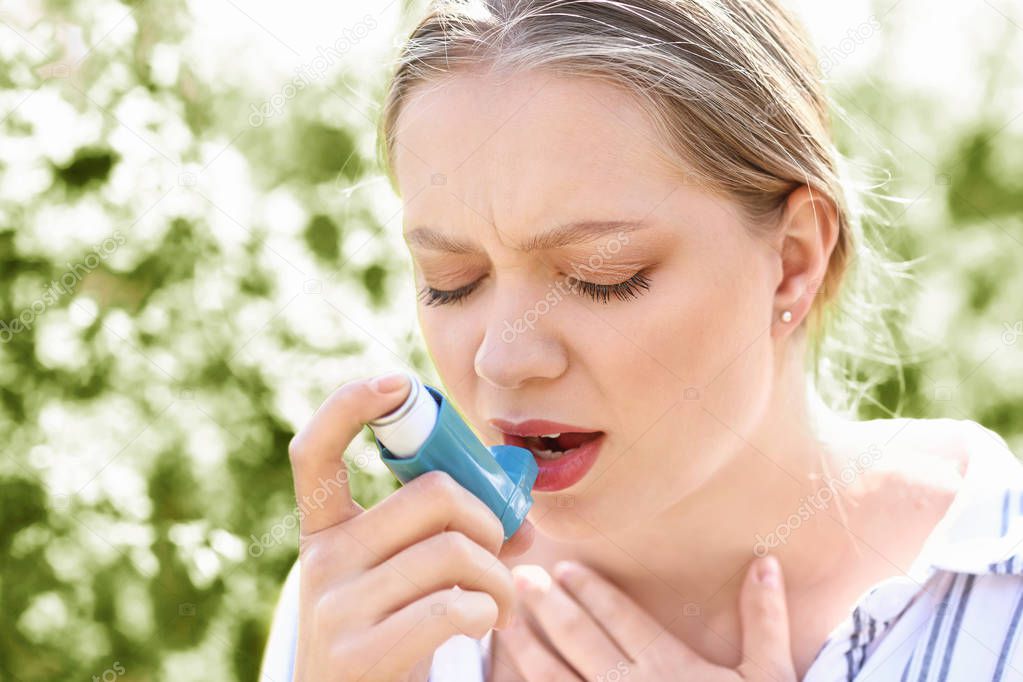 Woman with inhaler having asthma attack outdoors