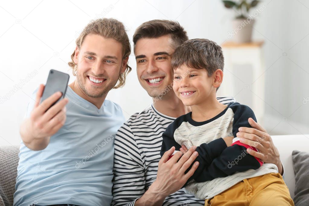 Happy gay couple taking selfie with adopted child at home