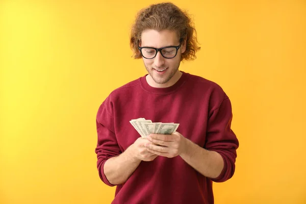 Happy young man with dollar banknotes on color background — Stock Photo, Image