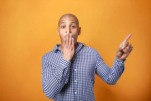 Shocked African-American man pointing at something on color background