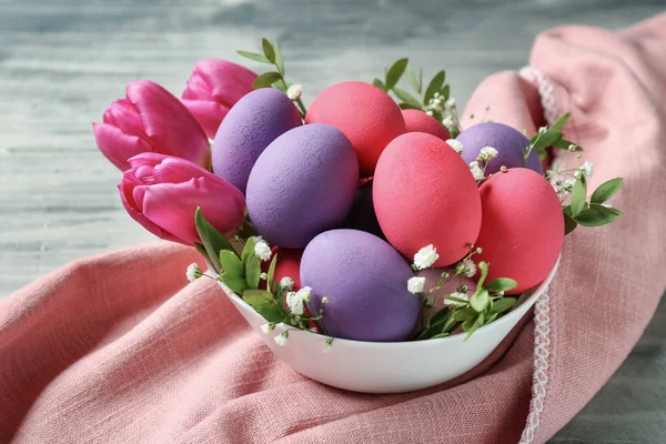 Tigela com belos ovos de Páscoa e flores na mesa cinza — Fotografia de Stock