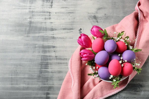 Tigela com belos ovos de Páscoa e flores na mesa cinza — Fotografia de Stock