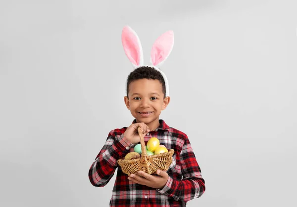 Liten afroamerikansk pojke med påskägg och kanin öron på ljus bakgrund — Stockfoto