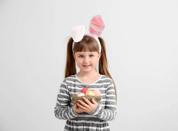Little girl with Easter eggs and bunny ears on light background — Stock Photo, Image