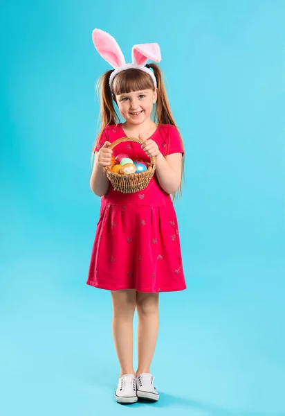 Renk arka planda Paskalya yumurtası ve tavşan kulakları sepeti ile küçük kız — Stok fotoğraf