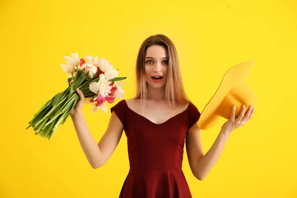 Surprised young woman with bouquet of beautiful tulips and hat on color background — Stock Photo, Image
